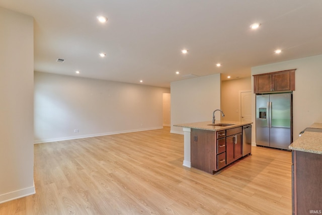 kitchen featuring an island with sink, sink, light stone counters, stainless steel appliances, and light hardwood / wood-style flooring
