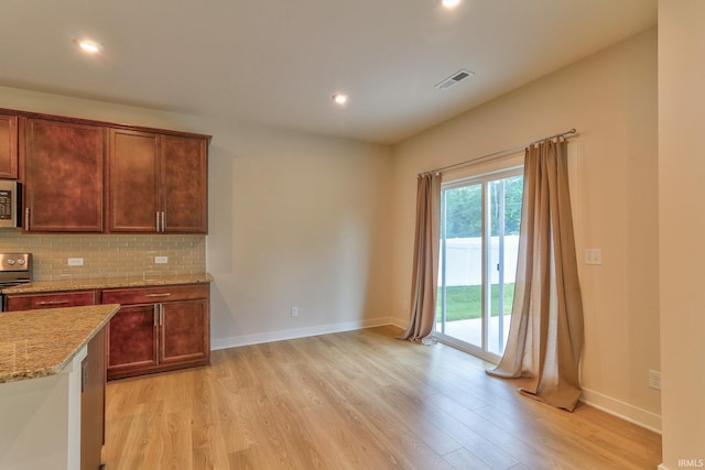 kitchen with stove, backsplash, light stone counters, and light hardwood / wood-style flooring