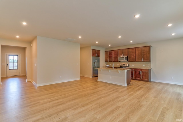 kitchen with stainless steel appliances, a breakfast bar area, a center island with sink, and light wood-type flooring