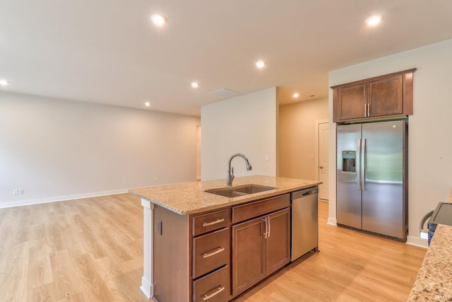 kitchen with sink, light stone counters, appliances with stainless steel finishes, a kitchen island with sink, and light hardwood / wood-style floors