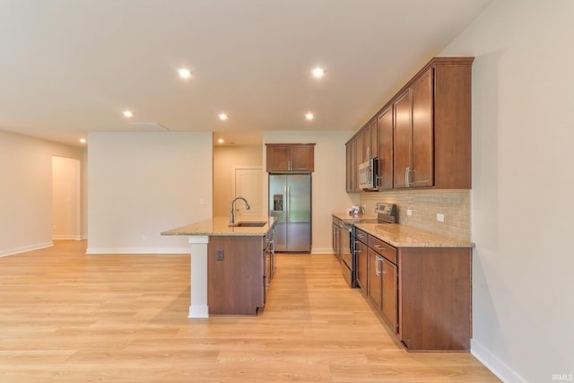 kitchen featuring stainless steel appliances, an island with sink, light stone counters, and light hardwood / wood-style floors