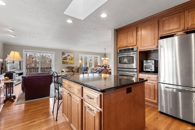 kitchen featuring appliances with stainless steel finishes, a skylight, light hardwood / wood-style floors, a kitchen island, and dark stone counters