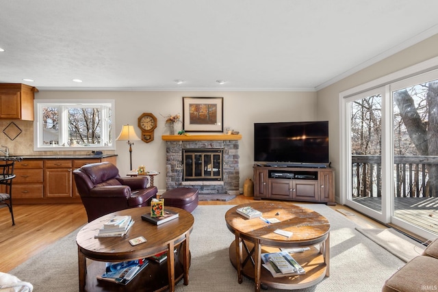 living room featuring a fireplace, crown molding, light hardwood / wood-style flooring, and a healthy amount of sunlight