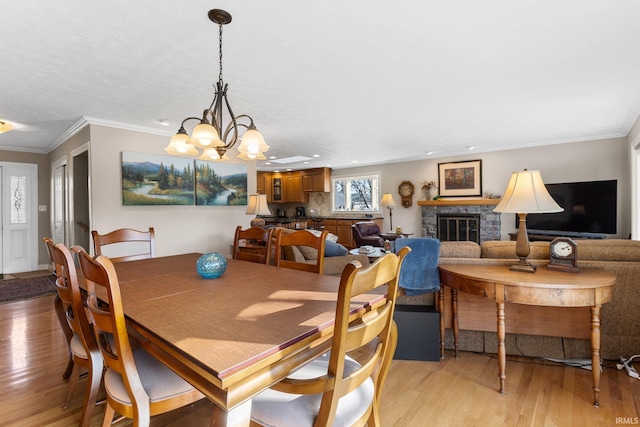 dining space with crown molding, an inviting chandelier, a fireplace, and light wood-type flooring