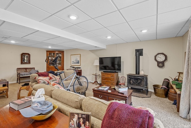 carpeted living room featuring a drop ceiling and a wood stove