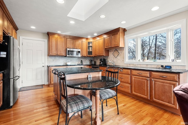 kitchen with dark stone countertops, light wood-type flooring, a skylight, and appliances with stainless steel finishes