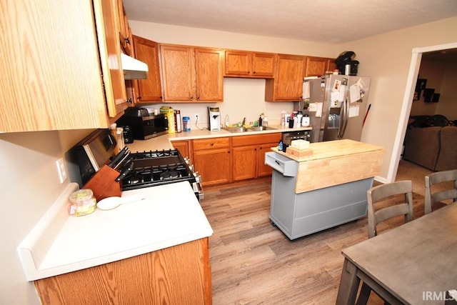 kitchen with stainless steel appliances, extractor fan, sink, and light hardwood / wood-style flooring