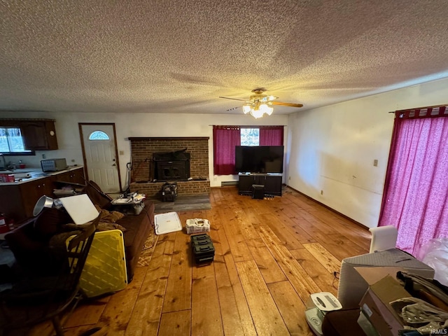 unfurnished living room featuring ceiling fan, wood-type flooring, a textured ceiling, and a wood stove