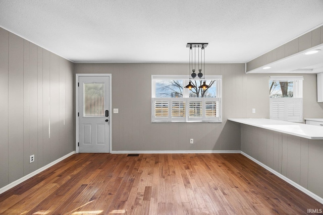 unfurnished dining area with hardwood / wood-style flooring, a wealth of natural light, a textured ceiling, and a chandelier