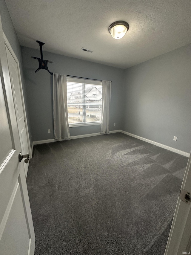 unfurnished room featuring dark carpet and a textured ceiling