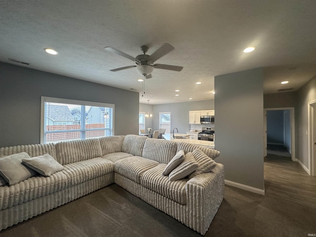 carpeted living room featuring ceiling fan, sink, and a textured ceiling