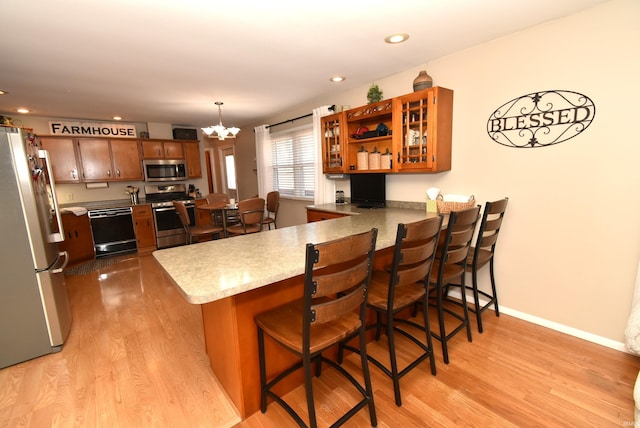 kitchen featuring a kitchen bar, decorative light fixtures, light hardwood / wood-style flooring, kitchen peninsula, and stainless steel appliances