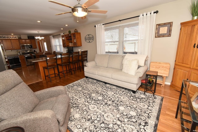 living room featuring ceiling fan with notable chandelier and light wood-type flooring