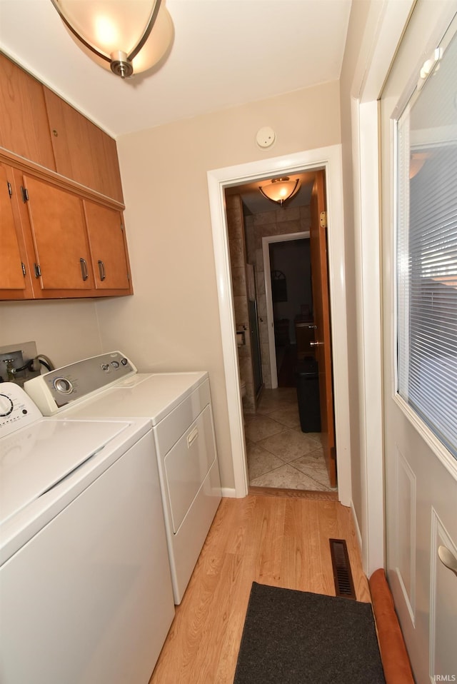 laundry area featuring light hardwood / wood-style flooring, washing machine and dryer, and cabinets