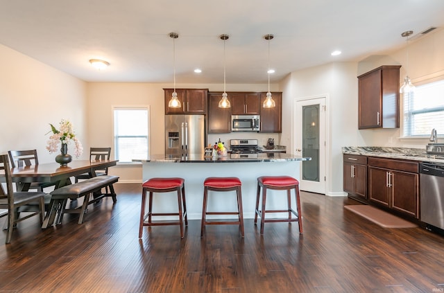 kitchen with a breakfast bar, light stone counters, a center island, appliances with stainless steel finishes, and pendant lighting