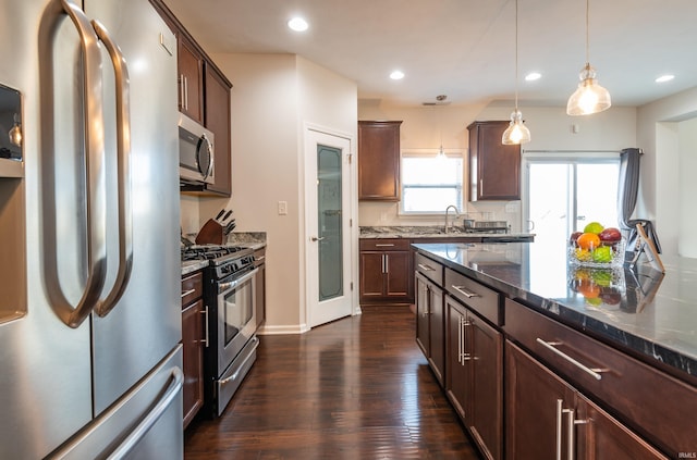 kitchen with dark hardwood / wood-style floors, dark stone countertops, hanging light fixtures, dark brown cabinetry, and stainless steel appliances