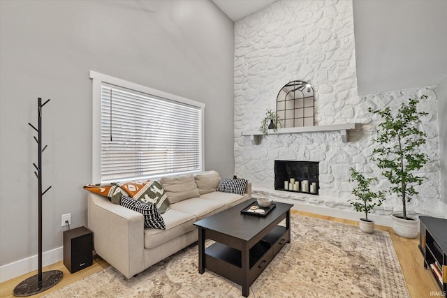 living room featuring a stone fireplace, a towering ceiling, and light hardwood / wood-style floors