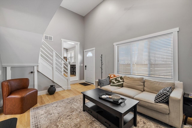 living room featuring a towering ceiling, a healthy amount of sunlight, and light hardwood / wood-style flooring