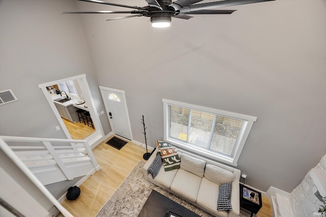 living room with hardwood / wood-style flooring, a towering ceiling, and ceiling fan