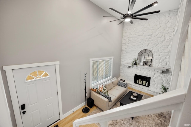 living room with a towering ceiling, a stone fireplace, ceiling fan, and light wood-type flooring