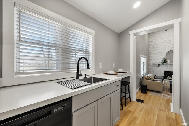 kitchen with sink, dishwasher, light hardwood / wood-style floors, a stone fireplace, and vaulted ceiling