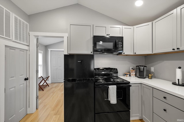 kitchen with lofted ceiling, gray cabinetry, black appliances, and light wood-type flooring