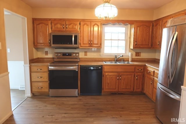 kitchen featuring hardwood / wood-style flooring, stainless steel appliances, decorative light fixtures, and sink