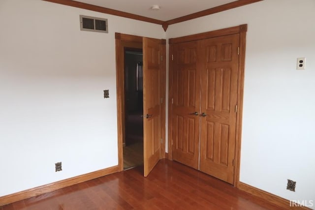 unfurnished bedroom featuring dark wood-type flooring, ornamental molding, and a closet