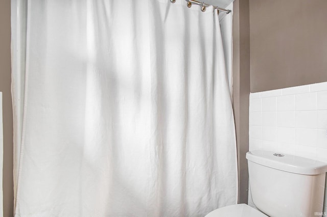 bathroom with toilet and tile walls