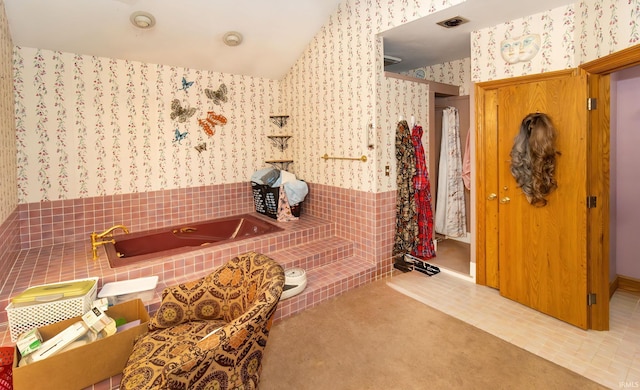 bathroom with lofted ceiling, a relaxing tiled tub, and tile patterned floors