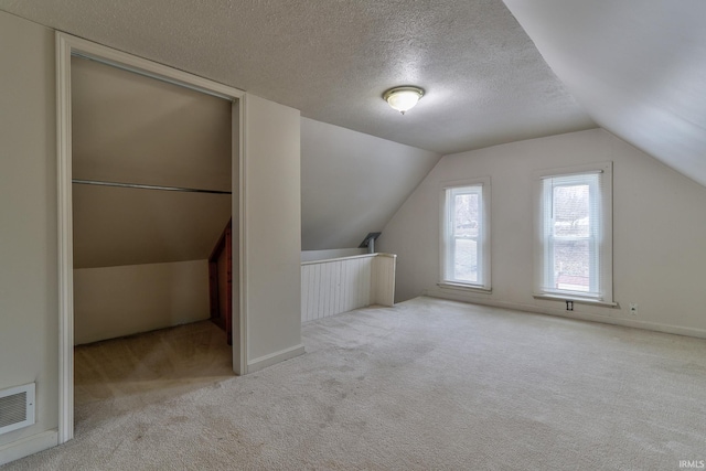 additional living space with lofted ceiling, light carpet, and a textured ceiling