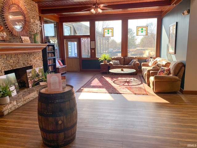 living room featuring beamed ceiling, a stone fireplace, hardwood / wood-style floors, and ceiling fan