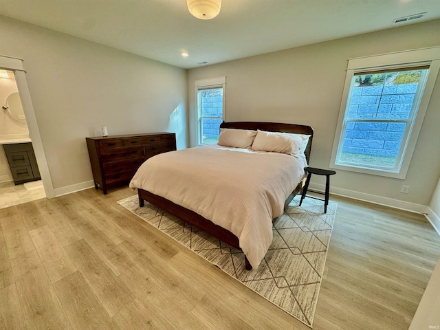 bedroom with ensuite bath, light hardwood / wood-style floors, and multiple windows