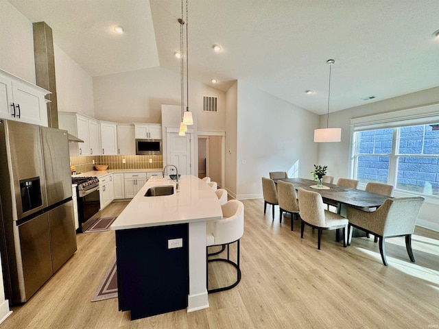 kitchen with sink, white cabinetry, hanging light fixtures, stainless steel appliances, and a kitchen island with sink