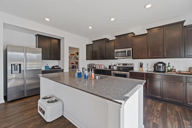 kitchen with sink, dark stone countertops, stainless steel appliances, dark wood-type flooring, and a center island with sink