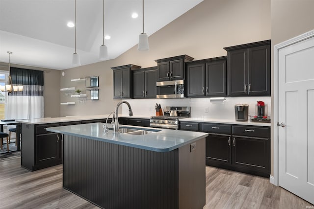 kitchen with sink, decorative light fixtures, light wood-type flooring, stainless steel appliances, and a kitchen island with sink