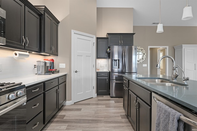 kitchen with pendant lighting, sink, backsplash, stainless steel appliances, and light hardwood / wood-style floors