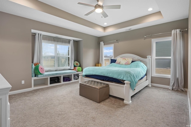 bedroom with a raised ceiling, light carpet, and multiple windows