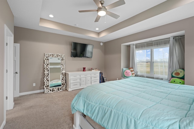 bedroom featuring ceiling fan, a tray ceiling, and light carpet