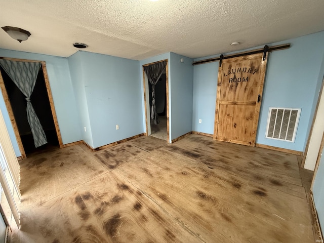 unfurnished bedroom with a barn door and a textured ceiling