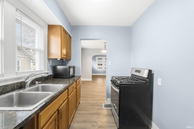 kitchen with dark stone counters, stainless steel gas range, sink, and light hardwood / wood-style flooring