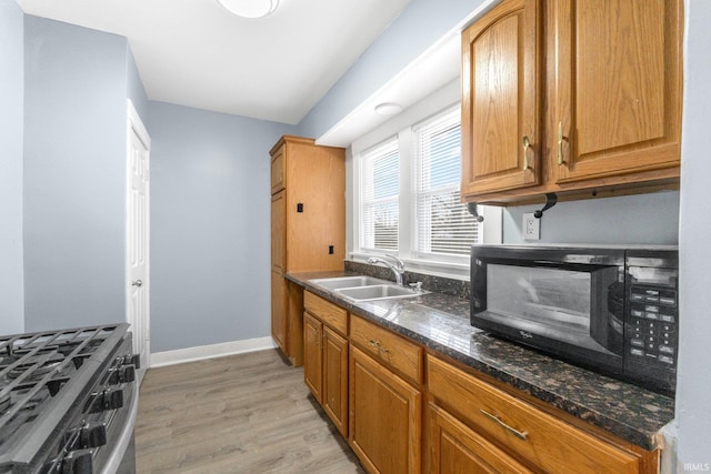 kitchen with dark stone counters, light hardwood / wood-style floors, sink, and stainless steel gas stove