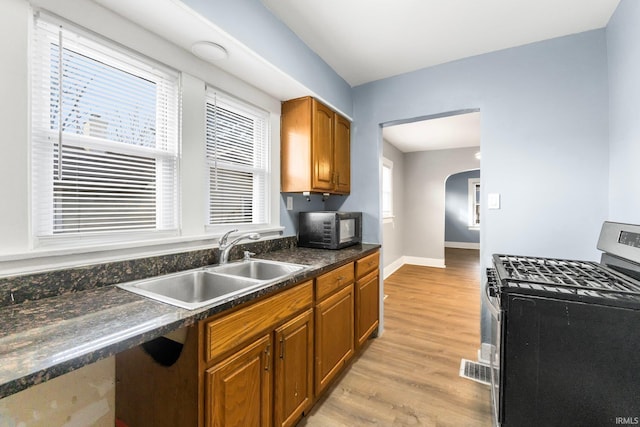 kitchen featuring gas range, sink, light wood-type flooring, and dark stone counters