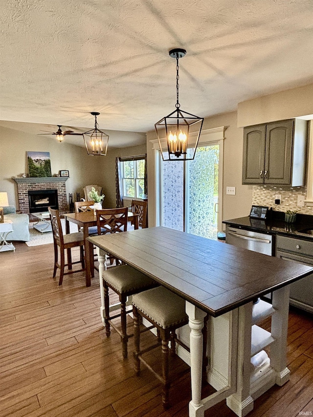 dining area featuring a brick fireplace, ceiling fan with notable chandelier, a textured ceiling, and dark hardwood / wood-style flooring