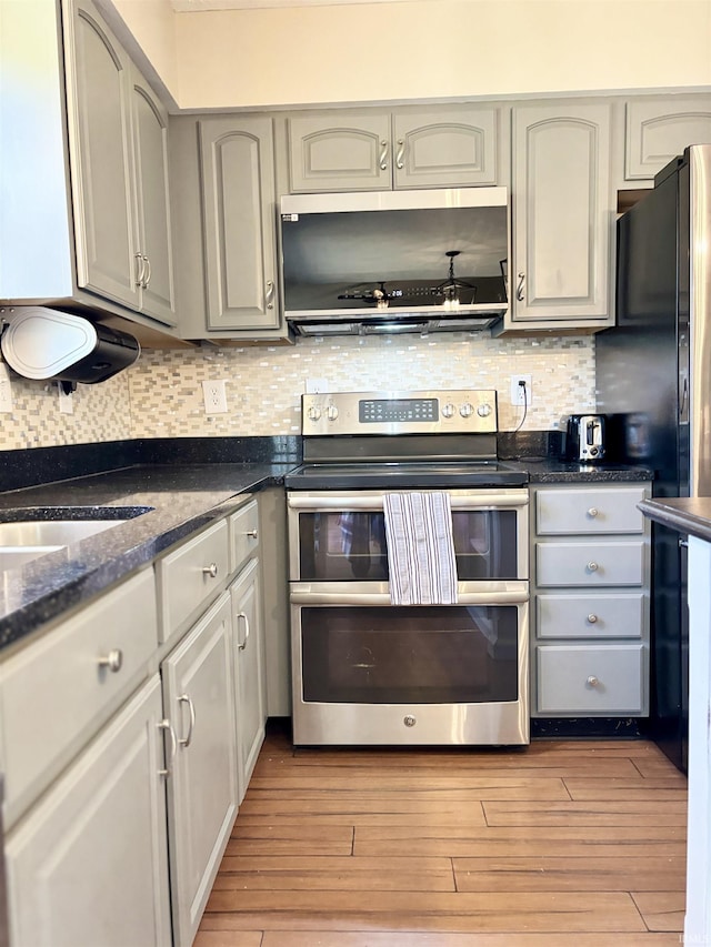 kitchen featuring gray cabinets, double oven range, range hood, light hardwood / wood-style floors, and decorative backsplash