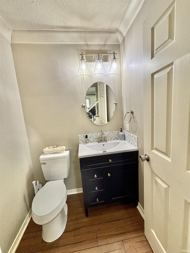 bathroom featuring wood-type flooring, ornamental molding, vanity, toilet, and a textured ceiling