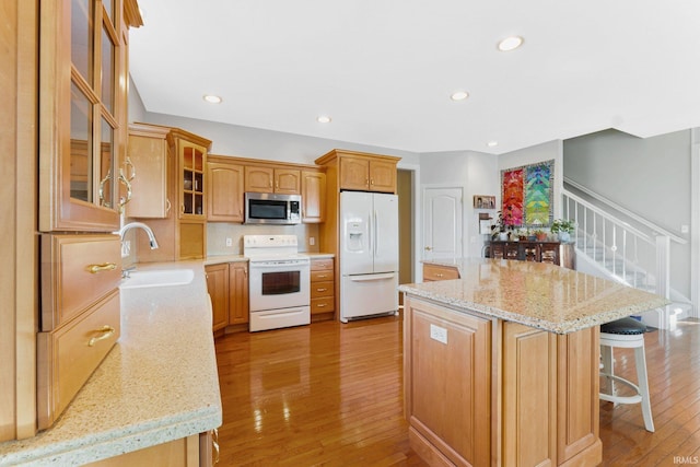 kitchen with sink, a kitchen island, white appliances, light stone countertops, and light hardwood / wood-style floors