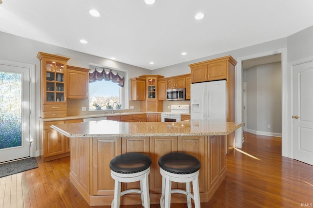 kitchen with white appliances, light hardwood / wood-style flooring, a center island, light stone counters, and decorative backsplash