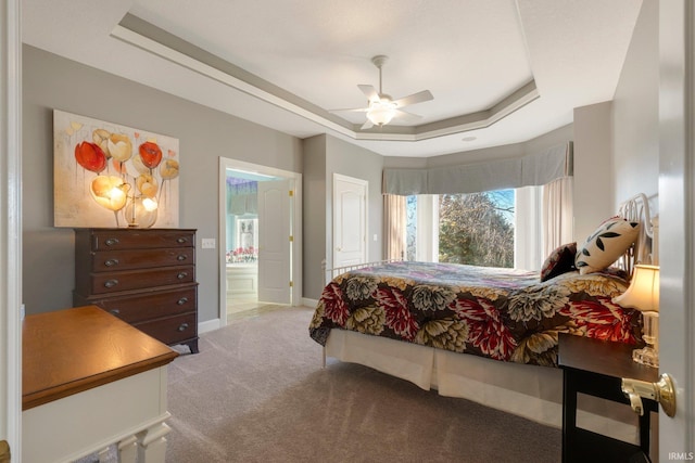 carpeted bedroom featuring ceiling fan, ensuite bathroom, and a raised ceiling