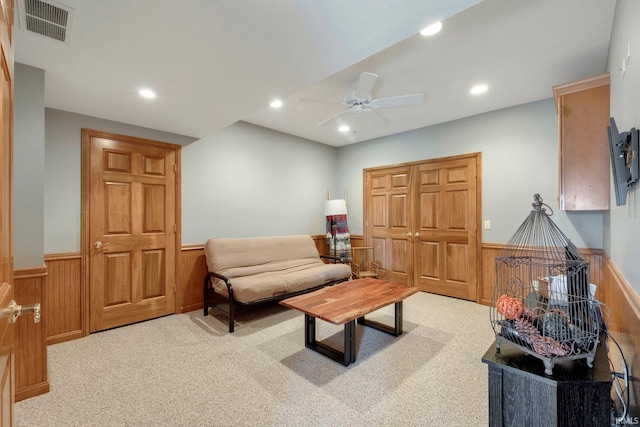 carpeted living room featuring ceiling fan and wood walls